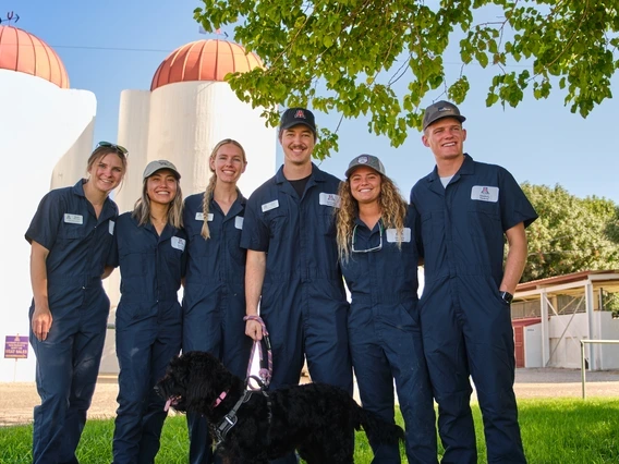A group of people in coveralls standing in front of siloes on a farm