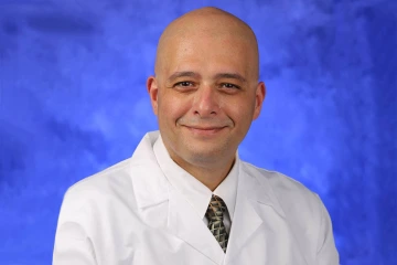 Portait of John Elfar, MD, in a white coat with a blue background